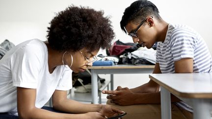 Des adolescents regardant leur téléphone dans une salle de classe (illustration). (DINOCO GRECO / MAXPPP)