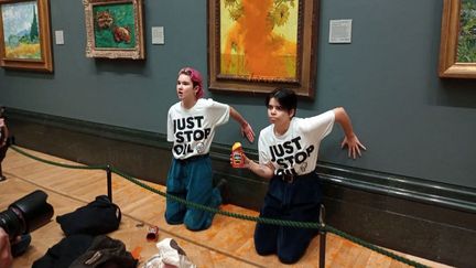 Deux militantes se collent à un mur de la National Gallery de Londres (Royaume-Uni), après avoir aspergé un tableau de soupe, le 14 octobre 2022. (JUST STOP OIL / HANDOUT / ANADOLU AGENCY / AFP)