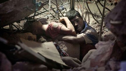 Le 24 avril 2013, le Rana Plaza, un b&acirc;timent haut de huit &eacute;tages qui abrite cinq usines textiles, s&rsquo;effondre dans la banlieue de Dhaka, capitale du Bangladesh. Pr&egrave;s de 1127 personnes meurent dans cette catastrophe, principalement des ouvriers. Au milieu des d&eacute;combres de cette usine textile mondiale, on d&eacute;couvre deux mois plus tard un couple enlac&eacute;. Personne ne connait le lien qui les unissait. Mais ces deux personnes sont mortes ensemble, prisonni&egrave;res des gravas. (PAUL SUMAN / AP / SIPA)