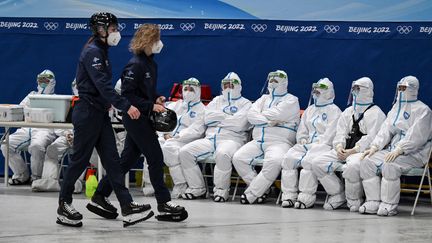 À bonne distance des hockeyeuses, les "minions" de Pékin s'offrent un rare moment de détente pour admirer le match, derrière leurs visières de plexiglas. L'autre grand défi de ces&nbsp;olympiades&nbsp;est d'éviter toute&nbsp;propagation du&nbsp;Covid-19.&nbsp;La Chine a mis au point un protocole sanitaire dantesque et créé une&nbsp;bulle tout autour des structures olympiques... et de leurs bénévoles. (ANNE-CHRISTINE POUJOULAT / AFP)