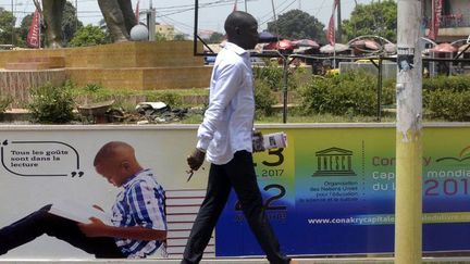 Un passant devant une affiche de l'Unesco pour la promotion de l'évènement «Conakry, capitale du livre» en 2017. (Cellou Binani/ AFP)