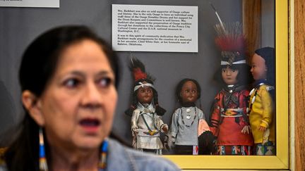 Des poupées traditionnelles exposées derrière la petite-fille de Mollie Burkhart, Margie Burkhart, au White Hair Memorial à Hominy, Oklahoma, le 29 septembre 2023. (CHANDAN KHANNA / AFP)