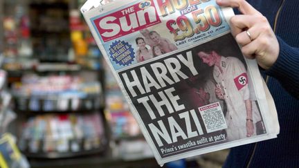 JANVIER 2005 - Scandale. Le prince Harry se retrouve en une des tabloïds pour avoir arboré un brassard avec une croix gammée lors d’une soirée déguisée. "Harry le nazi", titre le "Sun", avec une photo le montrant en costume, un verre dans une main et une cigarette dans l’autre. (GABRIEL BOUYS / AFP)