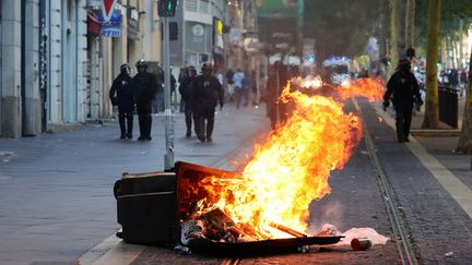 Des policiers anti-émeutes français montent la garde à côté d'une poubelle incendiée lors d'une manifestation contre la police à Marseille, dans le sud de la France, le 1er juillet 2023, après une quatrième nuit consécutive d'émeutes en France à la suite du meurtre d'un adolescent par la police. (CLEMENT MAHOUDEAU / AFP)