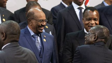 Le président soudanais Omar el-Béchir (à gauche, en costume bleu) salué par son homologue zimbabwéen Robert Mugarbe (de dos, en noir), président en exercice de l'Union africaine (UA), lors du 25e sommet de l'organisation panafricaine le 14 juin 2015. Le chef d'Etat soudanais s'est rendu en Afrique du Sud alors qu'il fait l'objet d'un mandat d'arrêt international lancé par la Cour pénale internationale (CPI). (AFP PHOTO / GIANLUIGI GUERCIA)