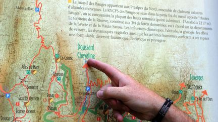 Un homme pointe la ville de Chevaline (Haute-Savoie) sur une carte, là, où a eu lieu en 2012 les meurtres de trois touristes britanniques et d'un cycliste. (PHILIPPE MERLE / AFP)