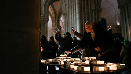 La lumière des cierges... et celle des téléphones portables brillent dans la cathédrale parisienne, en cette soirée du 24 décembre 2024. (JULIEN DE ROSA / AFP)