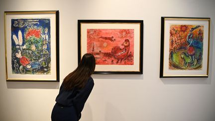 Une femme regarde des peintures originales inédites de l'artiste du XXe siècle, Marc Chagall, avant leur vente aux enchères en juin à Londres lors d'une présentation chez Christie's à Paris le 13 mai 2022.&nbsp; (CHRISTOPHE ARCHAMBAULT / AFP)