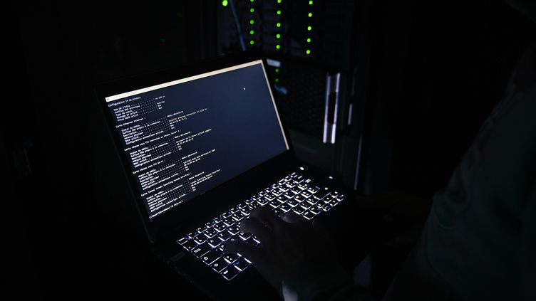 Illustration of a cyberattack with a person holding computer in front of servers.  (JOSSELIN CLAIR / MAXPPP)