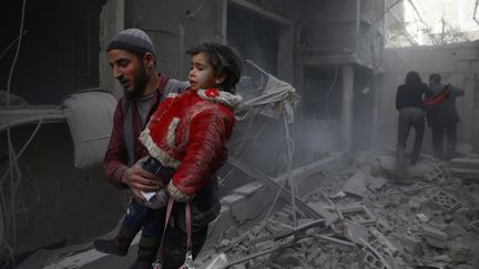 Un homme porte un enfant après un bombardement dans la ville de Douma, en Syrie, le 7 février 2018. (BASSAM KHABIEH / REUTERS)