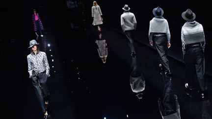 La femme Emporio Armani est aussi à l'aise en tenue sportive qu'en robe scintillante de soirée. Elle joue tantôt la femme de monde avec ses jupes droites mi longues, ses pantalons à pinces, ses vestes-boléro, sans oublier les touches de fourrure sur un col ou sur des manches et les noeuds noués à son cou ou à sa taille, et tantôt la jeune fille urbaine et active. Le vestiaire sportif et informel est présent avec des sneakers dorées et des pantalons courts moulants façon leggings. Y pointe aussi parfois un côté rebelle avec les chaînettes accrochées aux bottines ou bérets. Giorgio Armani joue sur les contrastes : masculin/féminin, noir contre blanc, matières classiques, tel velours, soie et flanelle combinées avec un PVC transparent utilisé pour confectionner des jupes (portées sur de chastes collants blancs) ou couvrir vestes et pantalons leur donnant une insolite brillance.
 (GIUSEPPE CACACE / AFP)