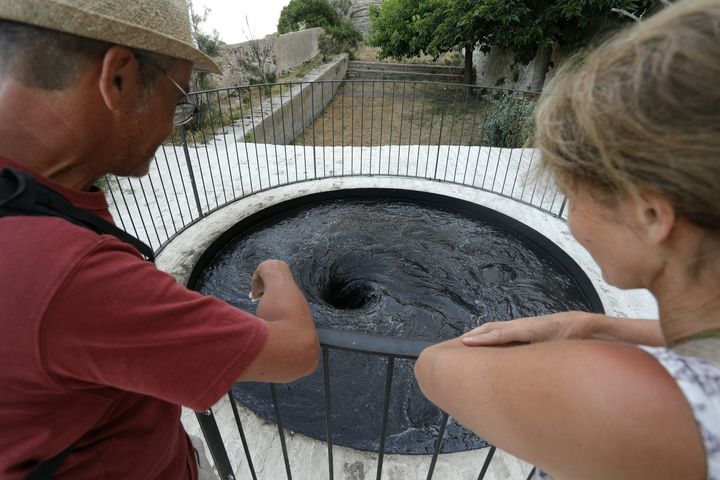 Deux touristes observent le tourbillon de la "Descension" d'Anish Kapoor, le 21 juin 2022 à Bonifacio (PASCAL POCHARD-CASABIANCA / AFP)