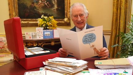 Le roi Charles III pose, le 21 février 2024, avec des cartes de vœux reçues après l'annonce de son cancer, à Buckingham Palace, à Londres (Royaume-Uni). (JONATHAN BRADY / POOL / AFP)