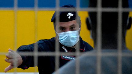 Un agent de sécurité italien devant des migrants dans un centre d'hébergement sur l'île de Lampedusa, le 14 mai 2021. (ALBERTO PIZZOLI / AFP)