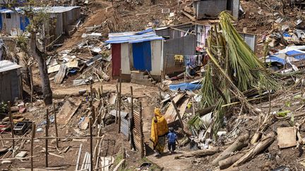 Une femme et un enfant marchent dans les décombres de Vahibe, en périphérie de Mamoudzou, le24 décembre 2024. (PATRICK MEINHARDT / AFP)