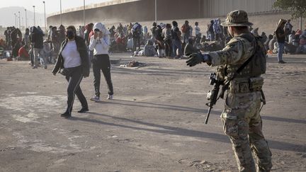 Un garde national au Texas et des migrants au niveau d'un camp de fortune situé entre le Rio Grande et la barrière frontalière entre les États-Unis et le Mexique, le 10 mai 2023 à El Paso, au Texas. (JOHN MOORE / GETTY IMAGES NORTH AMERICA / AFP)