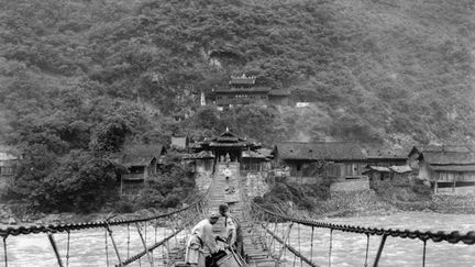 d’un pont suspendu en bois qui enjambe la rivière Da Du He entre la Chine et le Tibet. Sur la rive en face, une porte monumentale couverte à étage et, de part et d'autre, quelques maisons le long du fleuve.
 
 (Auguste François )