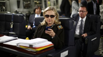 Hillary Clinton, alors secr&eacute;taire d'Etat, regarde son t&eacute;l&eacute;phone portable dans un avion &agrave; destination de Tripoli (Libye), le 18 octobre 2011. (KEVIN LAMARQUE / REUTERS)