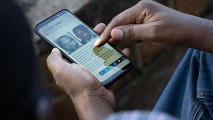 Un homme&nbsp;sur son smartphone à Kigali, la capitale rwandaise, le 18 mai 2020. On y aperçoit un article du "New Times" sur l'arrestation de Félicien Kabuga, l'un des principaux génocidaires&nbsp;qui échappaient encore à la justice. (SIMON WOHLFAHRT / AFP)