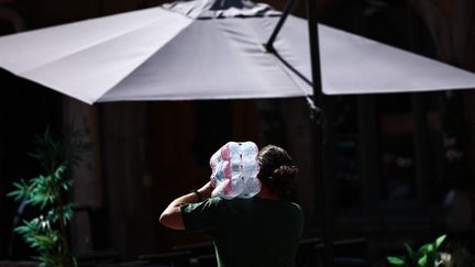 Un homme porte un pack de bouteilles d'eau, à Colmar (Haut-Rhin), le 21 août 2023. (SEBASTIEN BOZON / AFP)