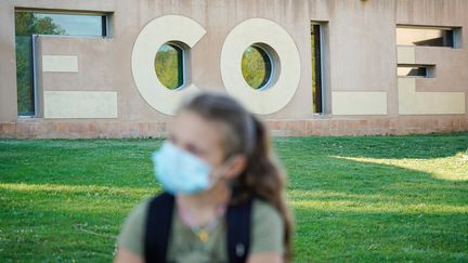 Une jeune fille portant un masque chirurgical devant une école. (MAXPPP)