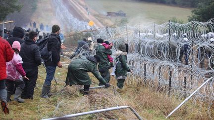 Des migrants à&nbsp;la frontière avec la Pologne dans la région de Grodno (Biélorussie), le 8 novembre 2021. De l'autre côté du mur de barbelés, la police polonaise. (LEONID SCHEGLOV / MAXPPP)