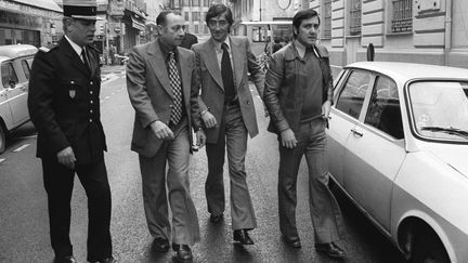 Albert Spaggiari (au centre, cravate noire), entour&eacute; de policiers et de son avocat, sur les lieux de son forfait, &agrave; Nice, lors d'une reconstitution,&nbsp;le 30 octobre 1976. (AFP)