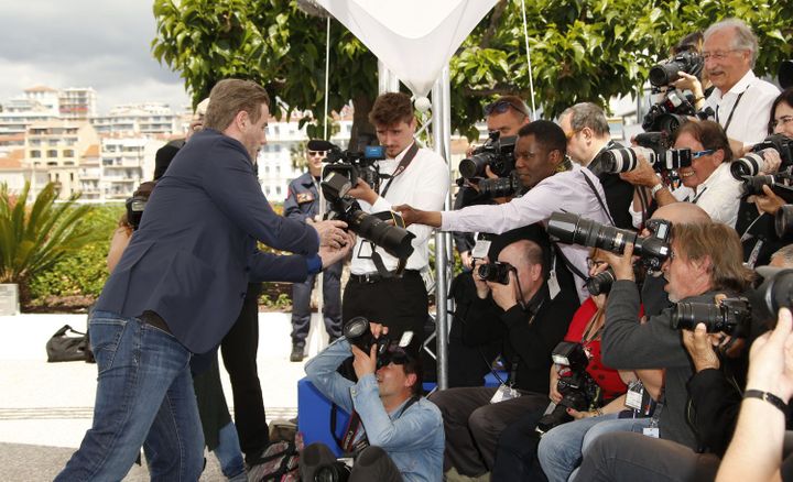 Le photographe Marcelo Nlele remet son appareil au comédien John Travolta en mai 2018 lors d'un photocall du Festival de Cannes. (Christophe Aubert )