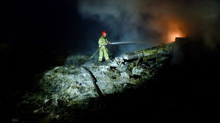 Un pompier tente d'&eacute;teindre les flammes qui &eacute;manent de la carcasse de l'appareil. (DOMINIQUE FAGET / AFP)