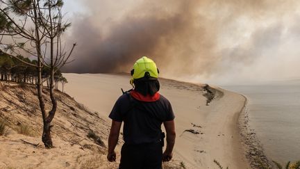 Un pompier devant la dune du Pilat alors que la fumée s'élève du feu de forêt de La Teste-de-Buch, le 18 juillet 2022. (THIBAUD MORITZ / AFP)