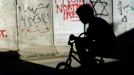 Un jeune cycliste palestinien devant le mur de séparation entre Jérusalem Ouest et Est (© AFP - Menahem Kahana)