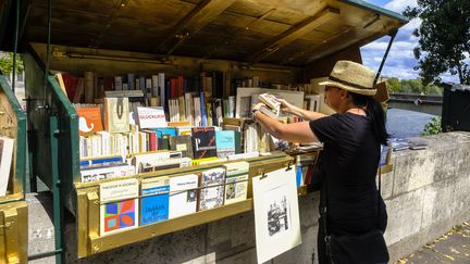 Une bouquiniste range son étalage de livres dans une des 900 boîtes "vert wagon" fixées au parapet le long de la Seine à Paris (France), le 28 août 2023. (JEAN-MICHEL DELAGE / HANS LUCAS / AFP)