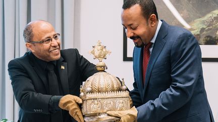 Sirak Asfaw (G) remet au Premier ministre éthiopien Abiy Ahmed la couronne du 18e siècle qu'il a conservée 21 ans aux Pays-Bas&nbsp; (- / ETHIOPIA PRIME MINISTER OFFICE)