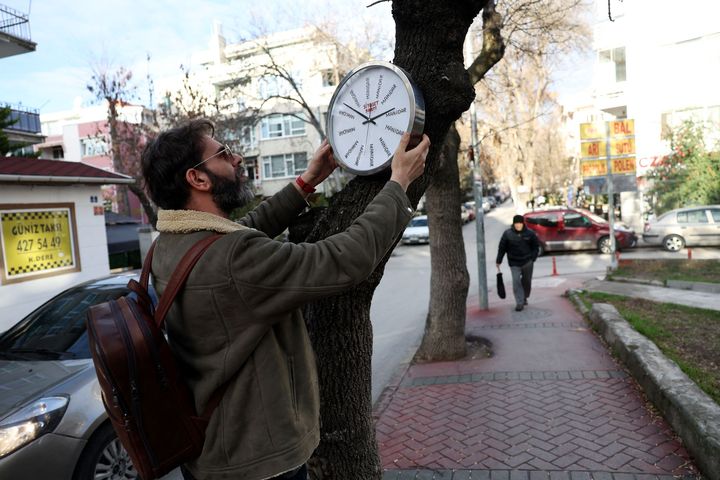 L'artiste de rue turc Hikmeti Tabiyeci installe l'une de ses créations intitulée "Horloge politique" sur un arbre, dans une rue d'Ankara, le 25 décembre 2023. (ADEM ALTAN / AFP)