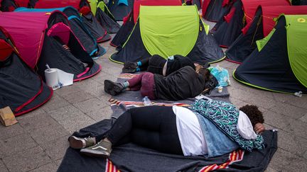 Des migrants sans-abri dorment sur le sol à côté de tentes installées la veille lors d'une action organisée par une association française devant l'Hôtel de Ville de Paris, le 25 juin 2021, pour souligner le sort des sans-abri dans le centre de Paris. (JOEL SAGET / AFP)