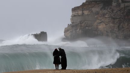 Un couple observe des vagues déferler sur une plage de Nazare, au Portugal (illustration). (FRANCISCO LEONG / AFP)