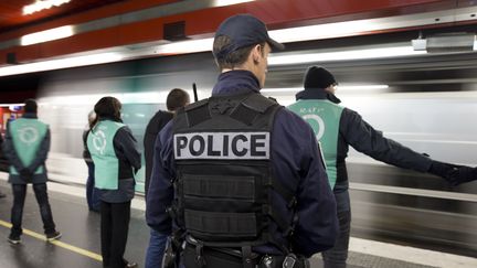 Un policier accompagne des agents de la RATP à la station de RER Auber, à Paris, le 30 décembre 2015. (KENZO TRIBOUILLARD / AFP)