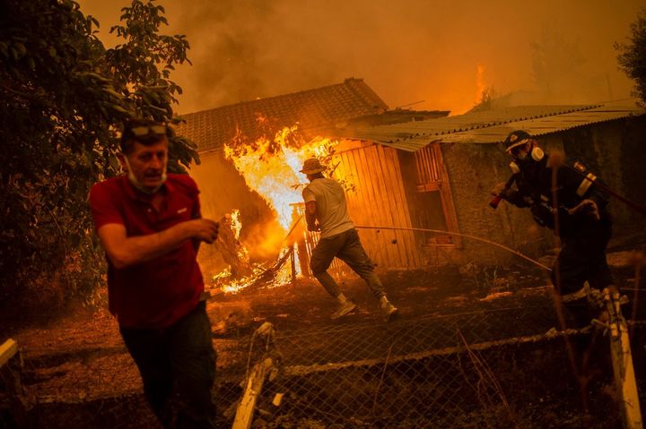 Un pompier et des habitants tentent d'éteindre les flammes, le 8 août 2021, à Pefki, sur l'île d'Eubée (Grèce). (ANGELOS TZORTZINIS / AFP)