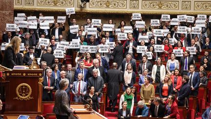 Des députés de la gauche brandissent des pancartes lors du déclenchement de l'article 49.3 pour adopter la réforme des retraites, le 16 mars 2023 à l'Assemblée nationale. (FRED DUGIT / MAXPPP)