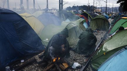 Un migrant&nbsp;se réchauffe les mains sur un feu qui peine à prendre&nbsp;après une tempête qui s'est abattue sur le camp d'Idomeni en Grèce, le 9 mars 2016.&nbsp; (DIMITAR DILKOFF / AFP)