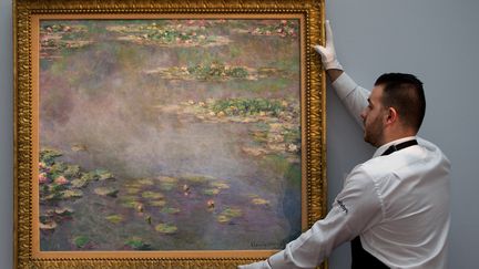 Un employ&eacute; de&nbsp;Sotheby's pose &agrave; c&ocirc;t&eacute; de l'&oelig;uvre de Claude Monet "Les&nbsp;Nymph&eacute;as", le 18 juin 2014. (ANDREW COWIE / AFP)