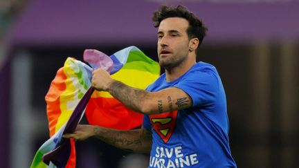 Un homme portant un tee-shirt "Save Ukraine" et un drapeau LGBTQ+ traverse la pelouse durant la rencontre du Mondial au Qatar, Portugal-Uruguay, le 28 novembre 2022. (ODD ANDERSEN / AFP)