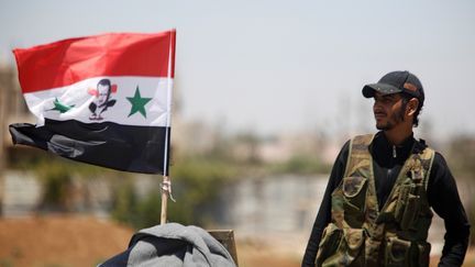 Un soldat de l'armée syrienne pose à côté d'un drapeau du régime syrien à Deraa le 10 juillet 2018. (OMAR SANADIKI / REUTERS)