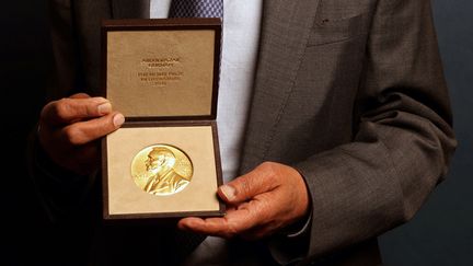 Médaille du Nobel de littérature dans les mains du lauréat 2021, le romancier britannique Abdulrazak Gurnah, lors d'une cérémonie à la résidence de l'ambassadeur de Suède à Londres le 6 décembre 2021 (ADRIAN DENNIS / AFP)