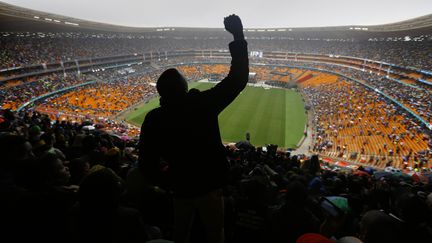 Un homme l&egrave;ve le poing lors du discours de Barack Obama dans le stade de&nbsp;Johannesburg (Afrique du Sud), le 10 d&eacute;cembre 2013, o&ugrave; se tient la c&eacute;r&eacute;monie d'hommage &agrave; Nelson Mandela. (YANNIS BEHRAKIS / REUTERS)