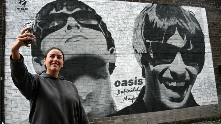 Une fan fait un selfie devant une fresque représentant les frères Gallagher, du groupe Oasis, qui a annoncé en 2024 une tournée historique dès l'été 2025. (PAUL ELLIS / AFP)