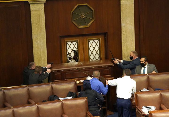 Des officiers de police pointent leurs armes en direction de manifestants qui tentent de pénétrer par la force dans la Chambre des représentants, à Washington, mercredi 6 janvier 2021.&nbsp; (DREW ANGERER / GETTY IMAGES / AFP)