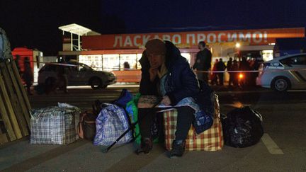 Un passager est assis sur des sacs alors qu'un convoi de 30 bus transportant des évacués de Marioupol et Melitopol arrive au centre d'enregistrement de Zaporijié, le 1er avril 2022. (EMRE CAYLAK / AFP)