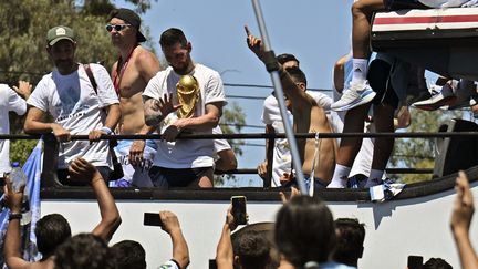 Emiliano Martinez (torse nu) et Lionel Messi portant le trophée de la Coupe du monde, le 20 décembre 2022 à Buenos Aires. (LUIS ROBAYO / AFP)