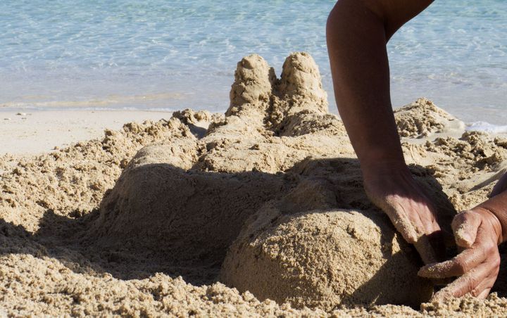 Sadika Keskes en train de sculpter un corps de sable sur la plage de Lampedusa (Clara Puente)